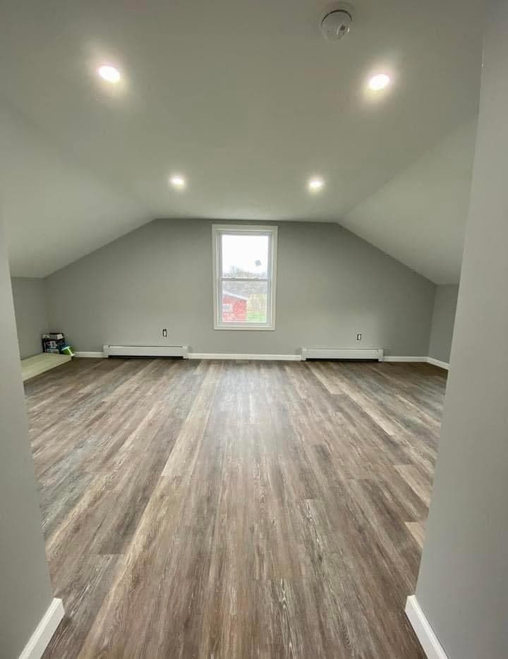 Empty attic room addition with vaulted ceiling, gray walls, and wood flooring