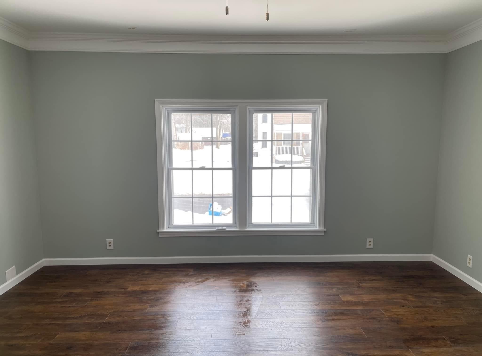 Empty room with sage green walls, dark hardwood floors, and white-trimmed windows