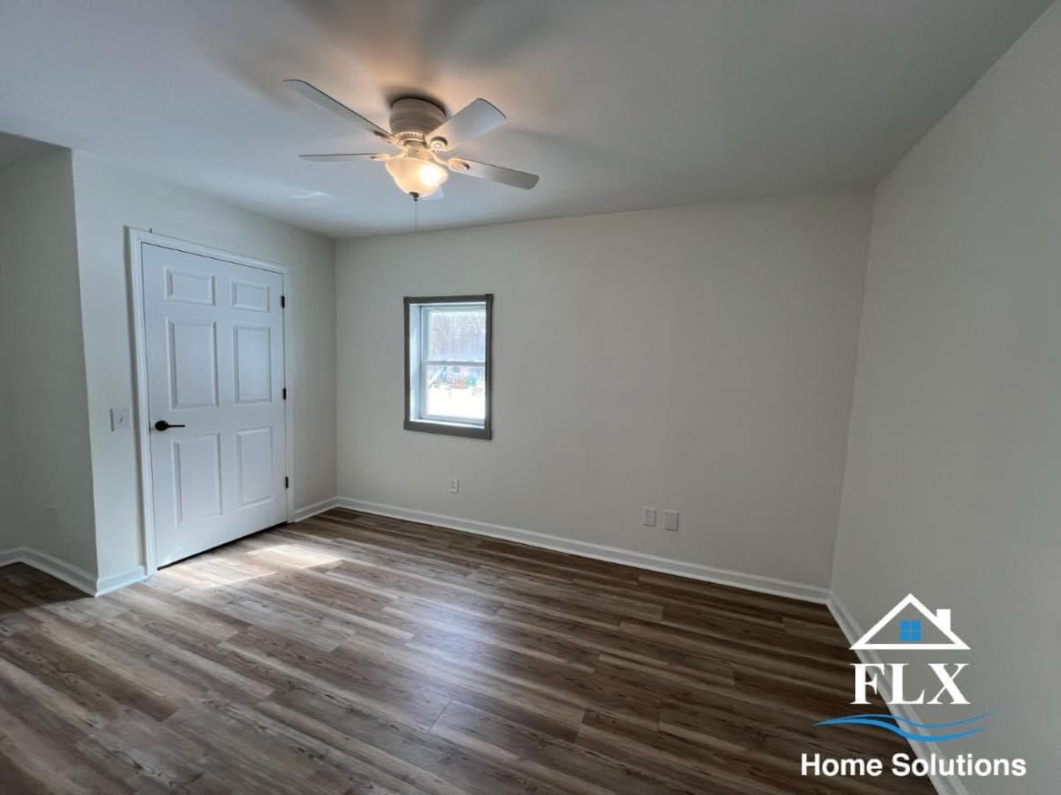 Empty bedroom with white walls, wood laminate flooring, ceiling fan, and window