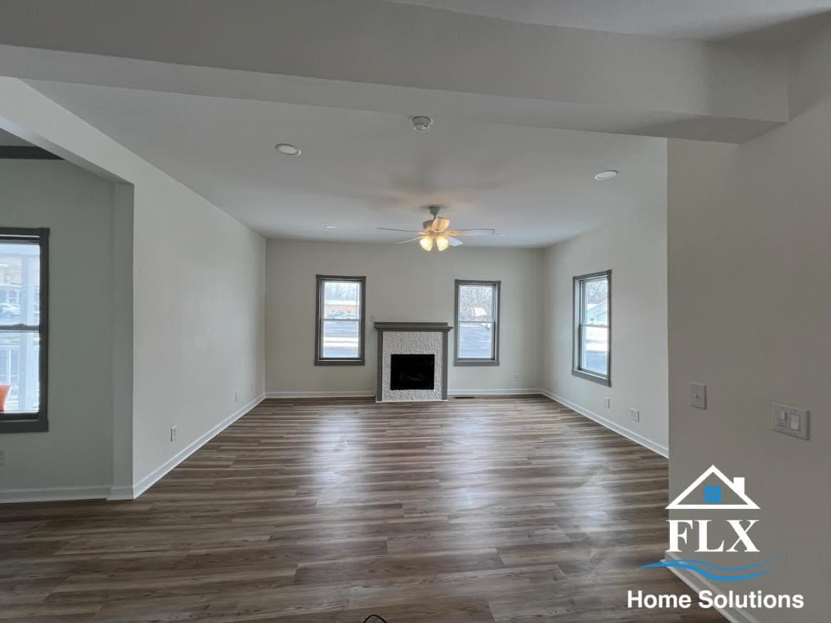 Empty living room addition with wood floors, fireplace, and three windows