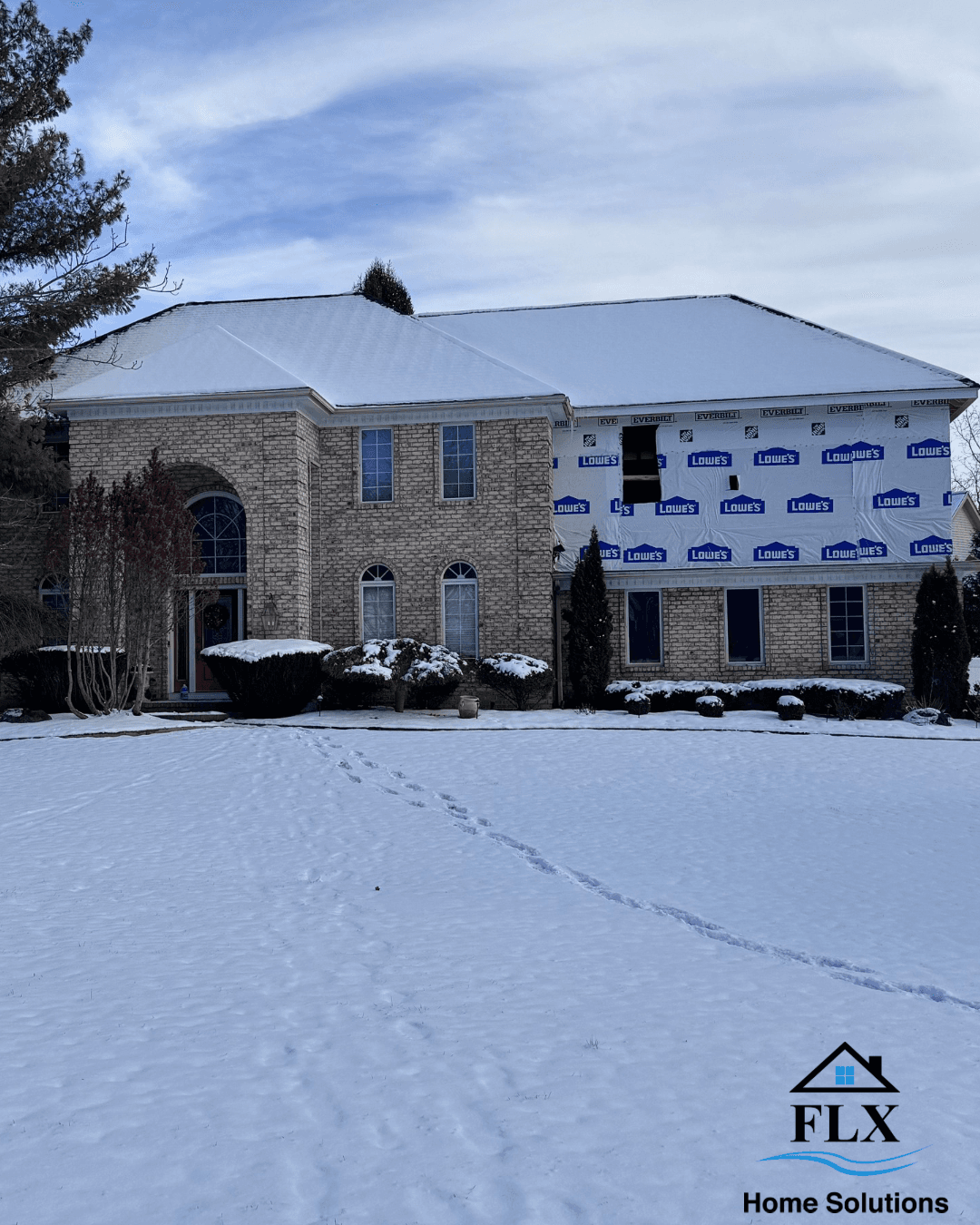 Large brick home with snow-covered addition wrapped in Lowe's house wrap