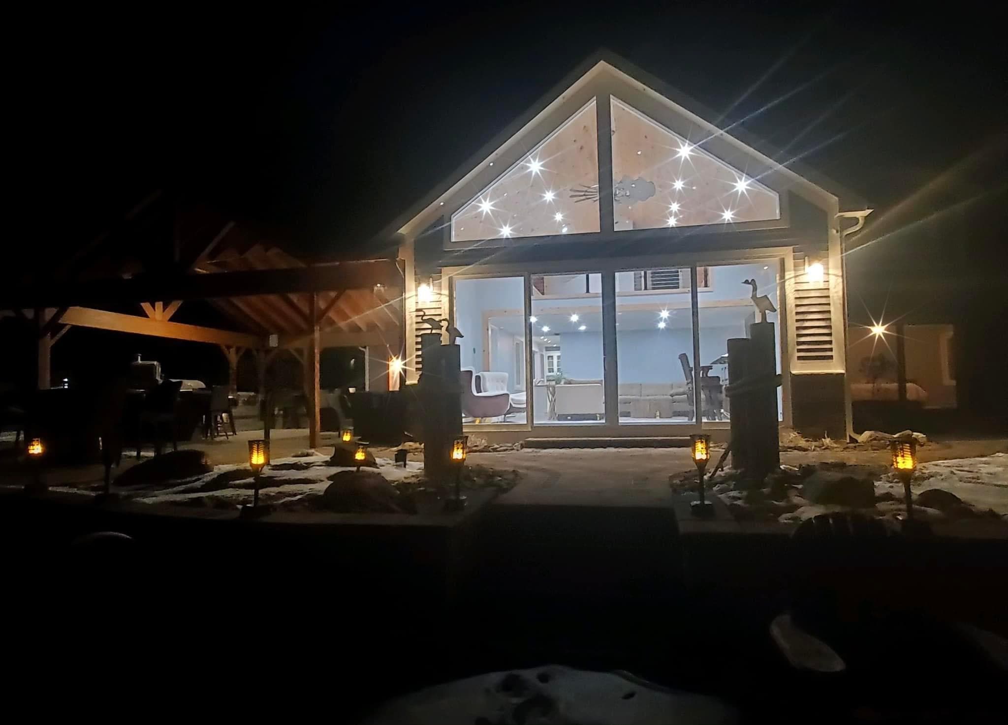 Illuminated modern home addition with triangular windows and outdoor patio at night