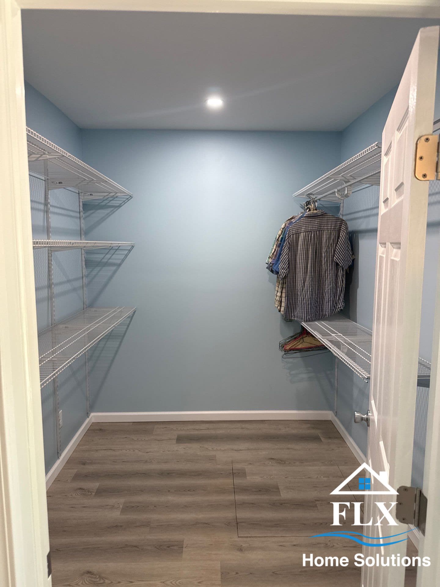 Walk-in closet with light blue walls, wire shelving, and laminate flooring
