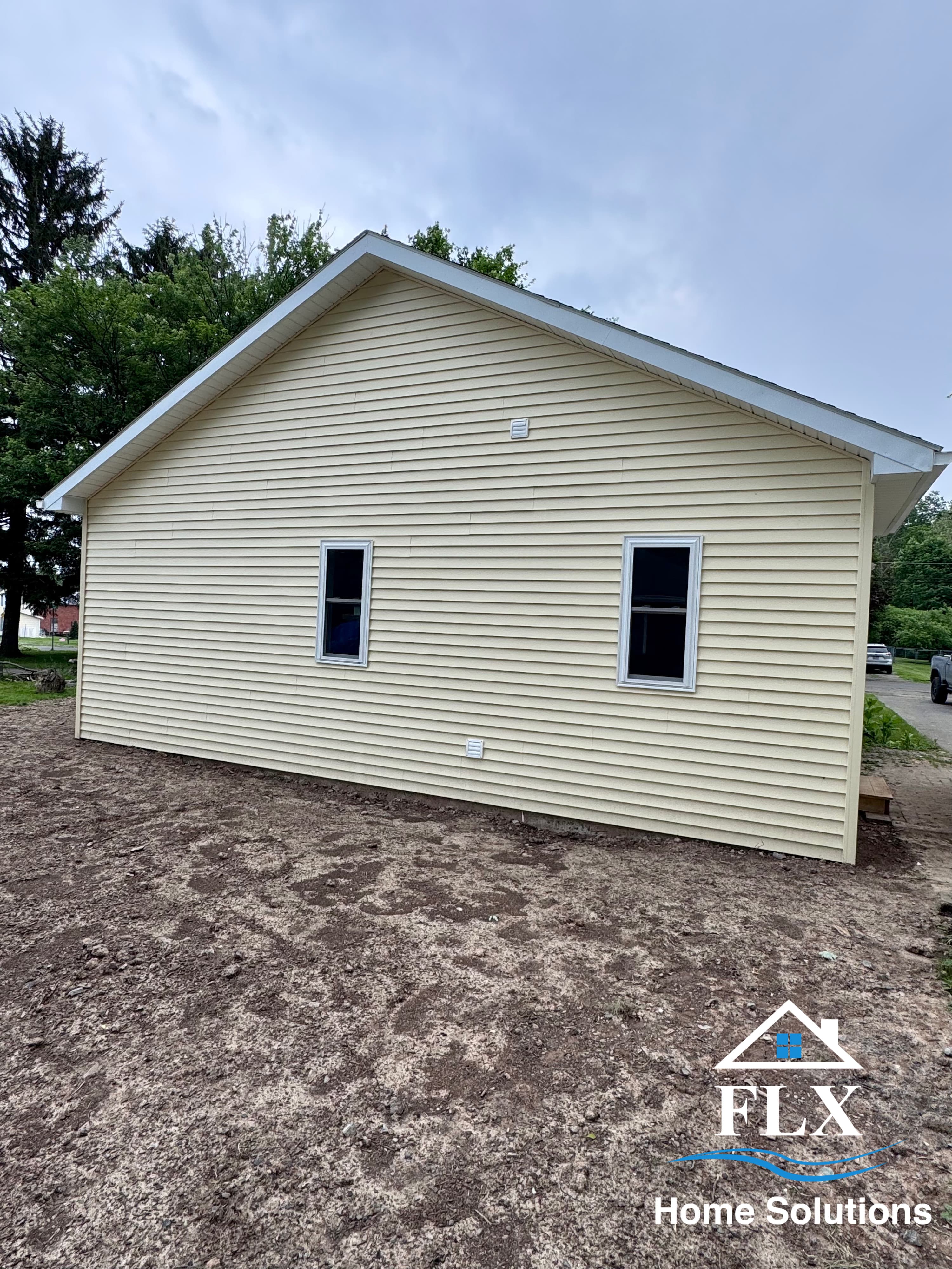 Newly constructed home addition with yellow vinyl siding and two windows
