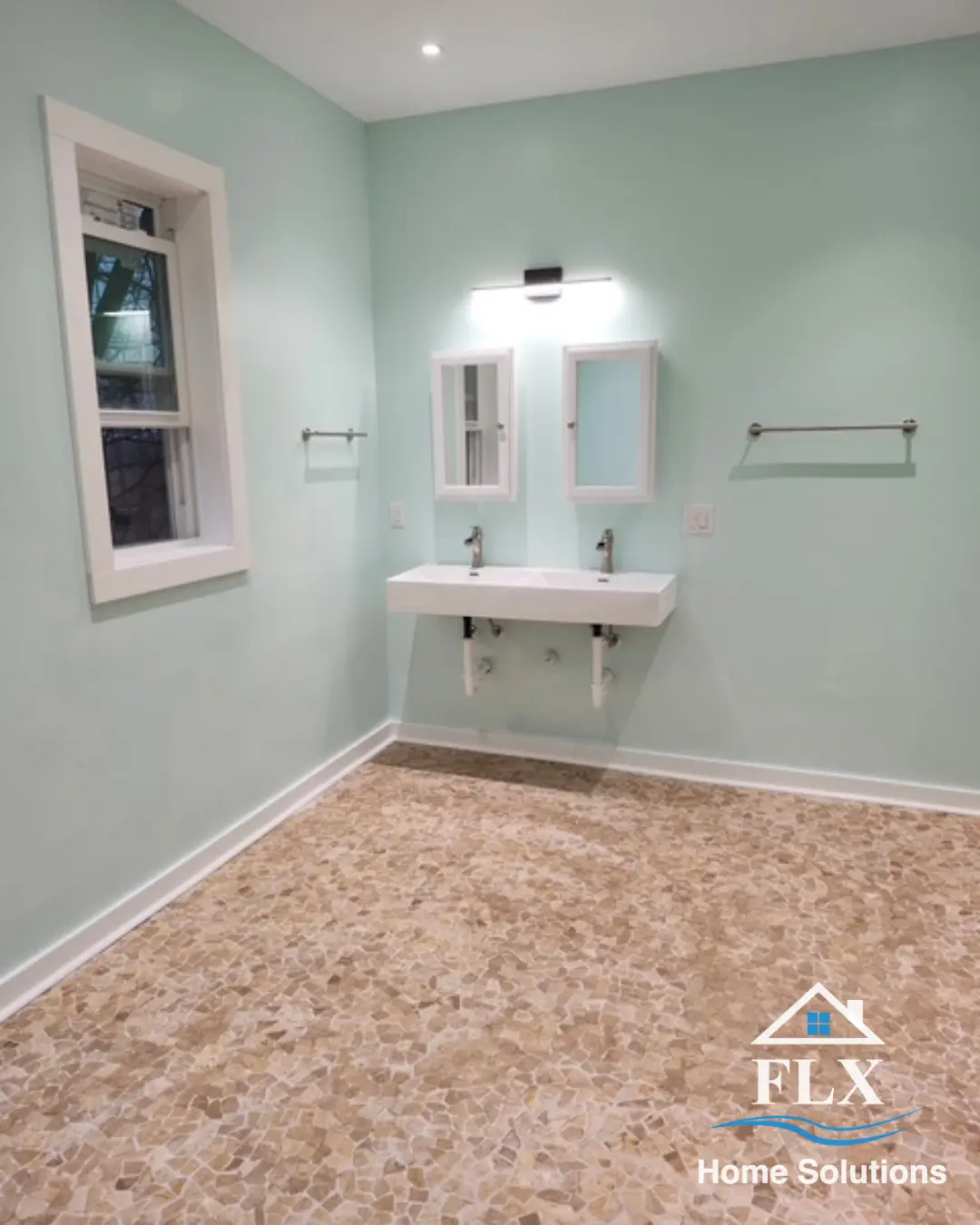 Renovated bathroom with wall-mounted dual sink, medicine cabinets, mint green walls, and pebble stone flooring