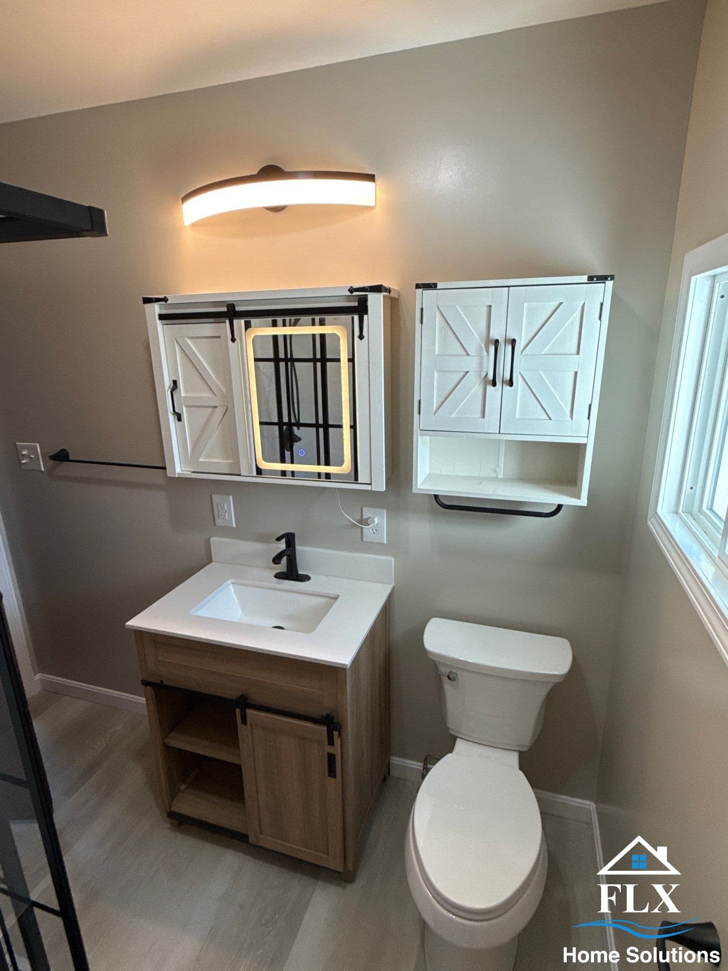 Completed bathroom with wood vanity, sliding barn door mirror, white toilet, and wall-mounted cabinet