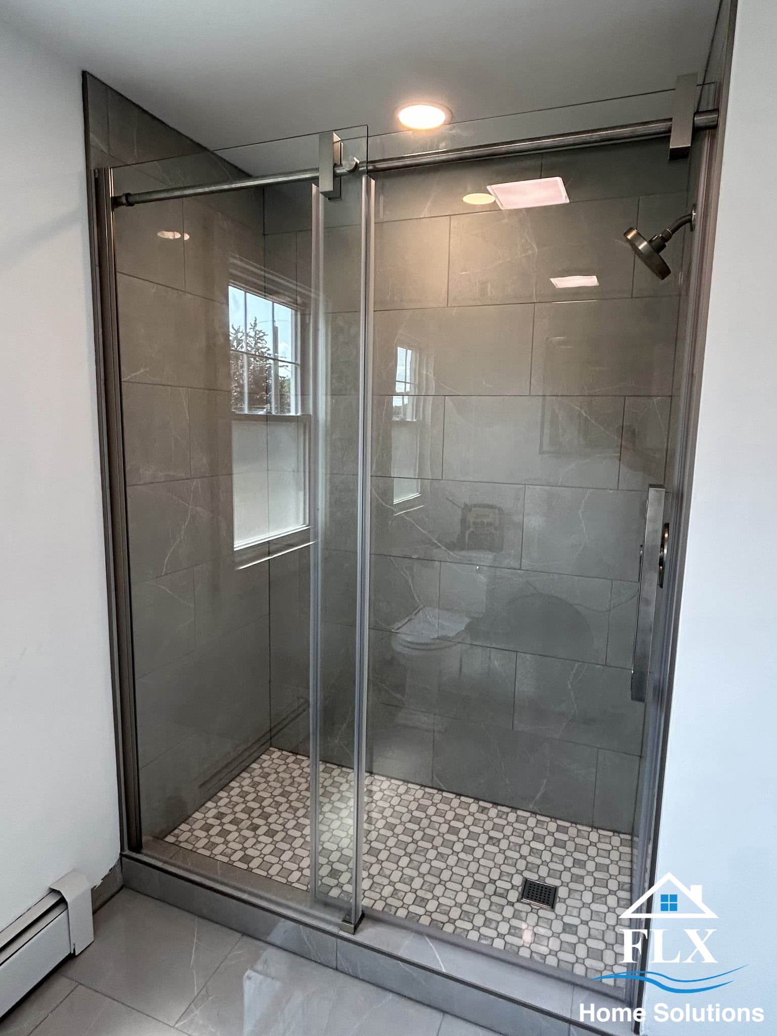 Modern walk-in shower with gray tile walls, glass doors, and mosaic floor
