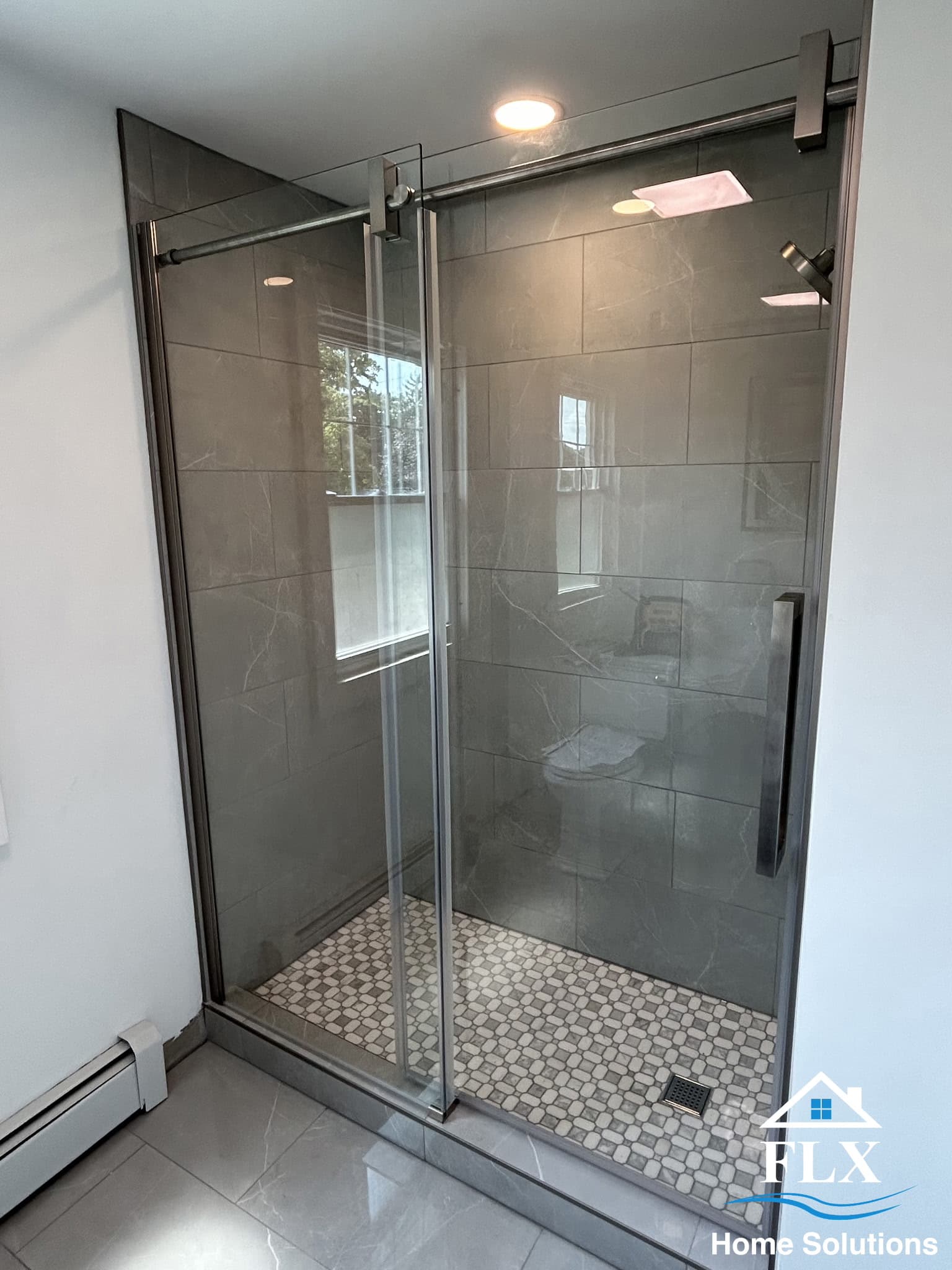 Modern walk-in shower with gray tile walls, pebble floor, and frameless glass doors