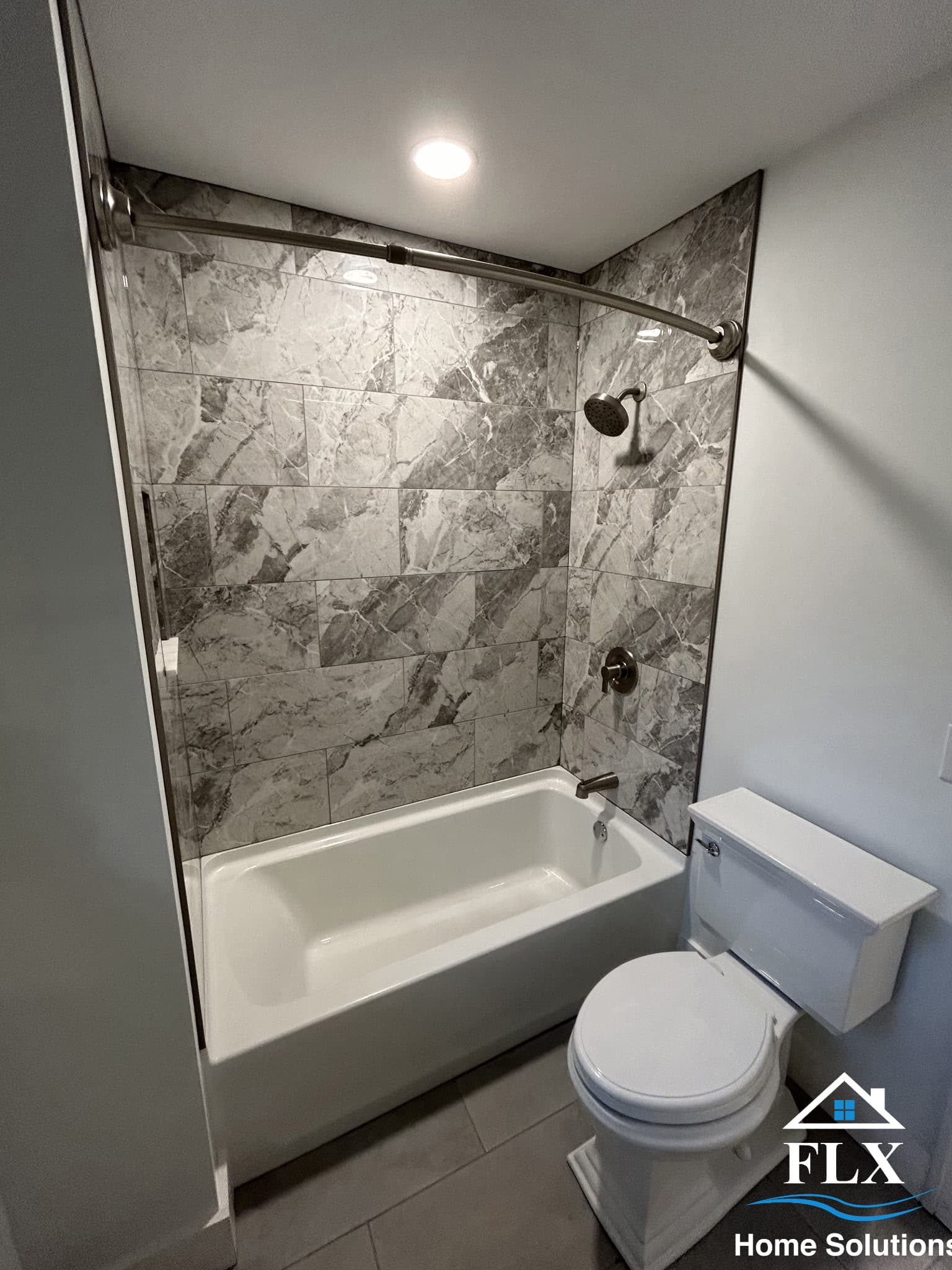 Modern bathroom with gray marble tile surround, white tub, and glass door