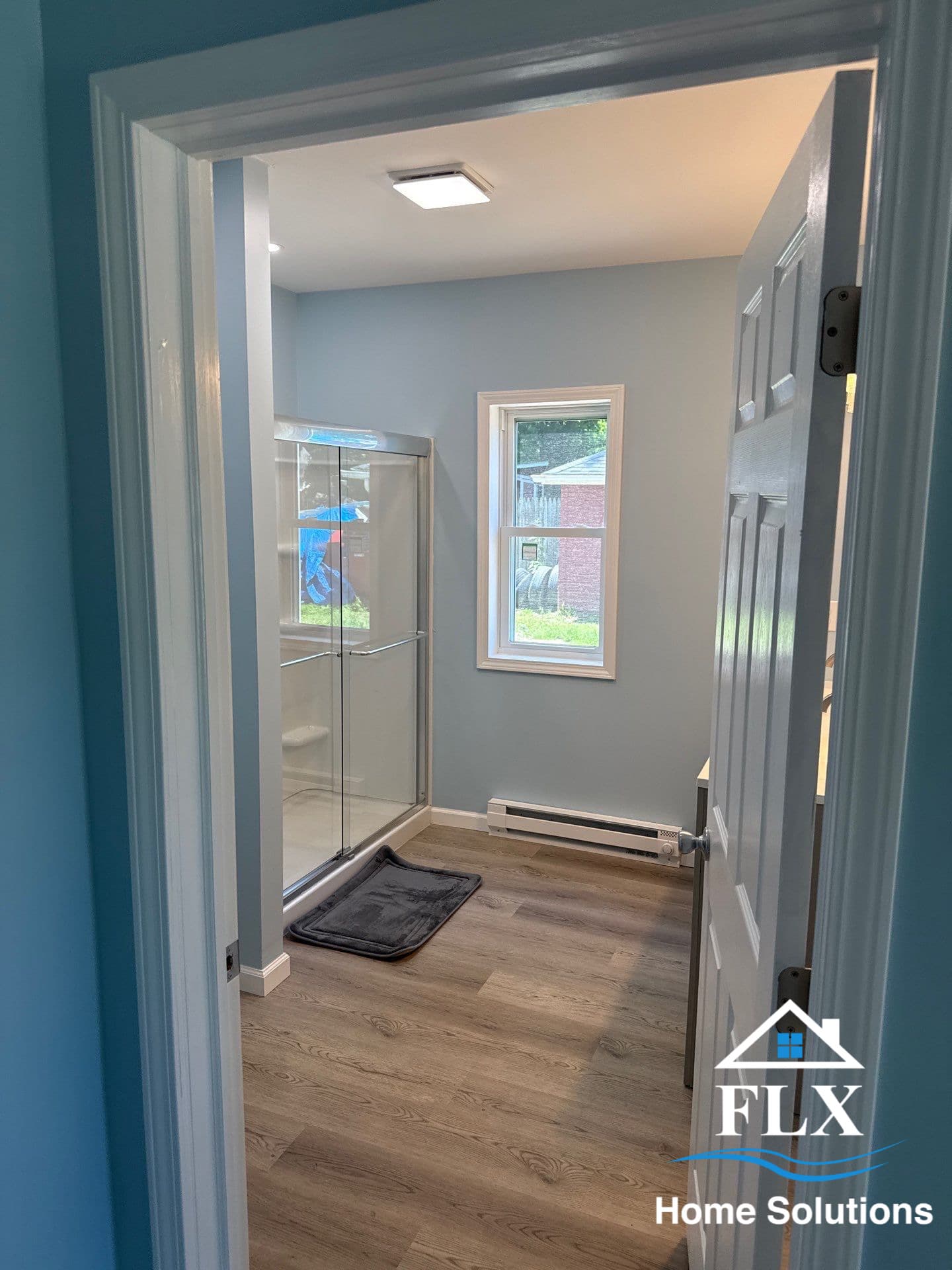 Renovated bathroom with glass shower enclosure and light wood flooring