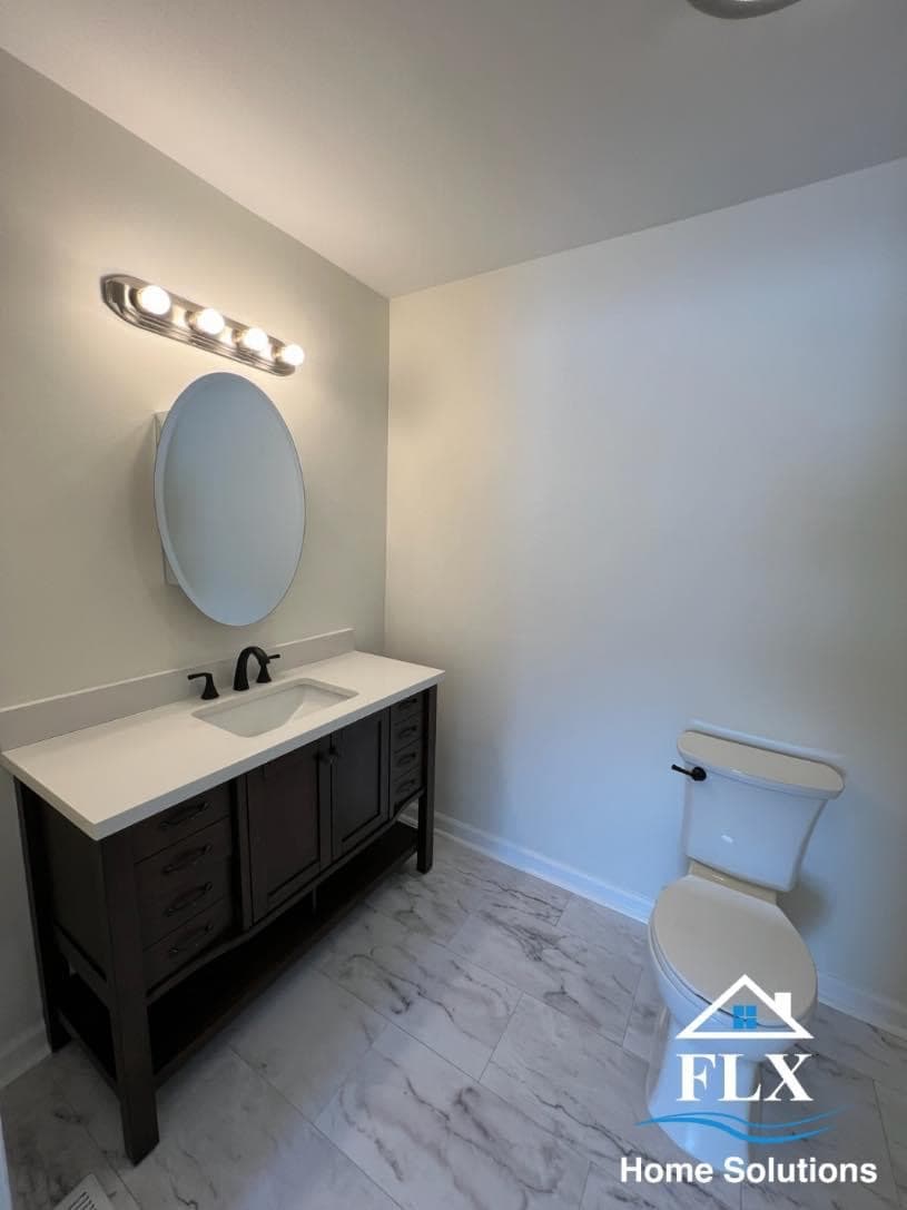 Modern bathroom with dark vanity, oval mirror, marble-look tile flooring, and white toilet