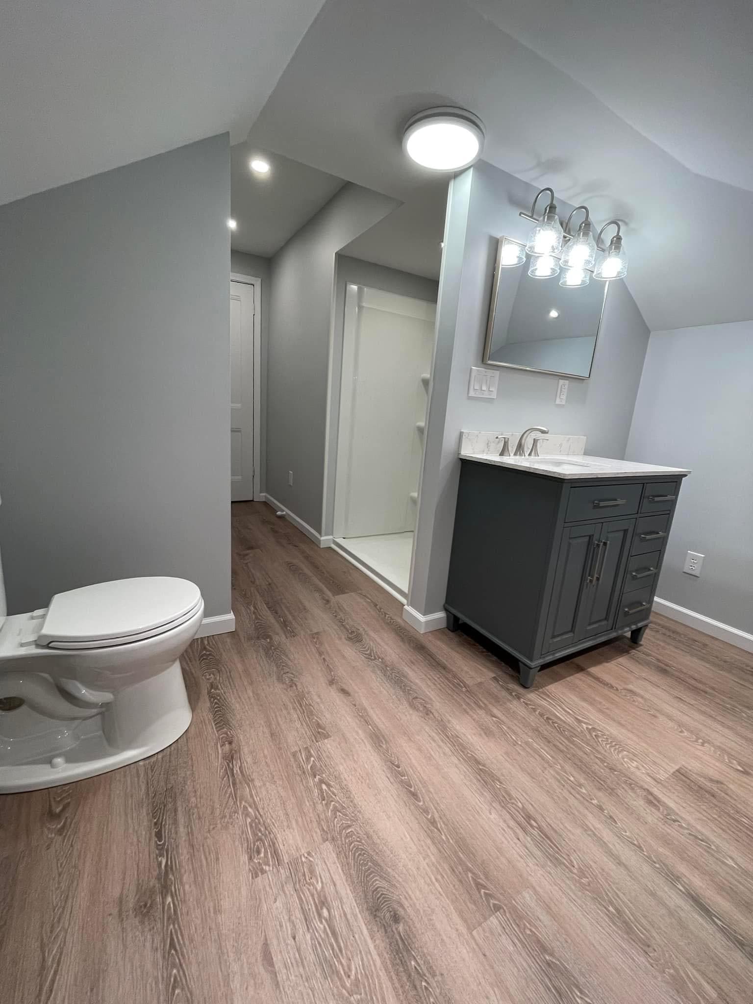 Remodeled bathroom with gray vanity, wood-look flooring, and vaulted ceiling