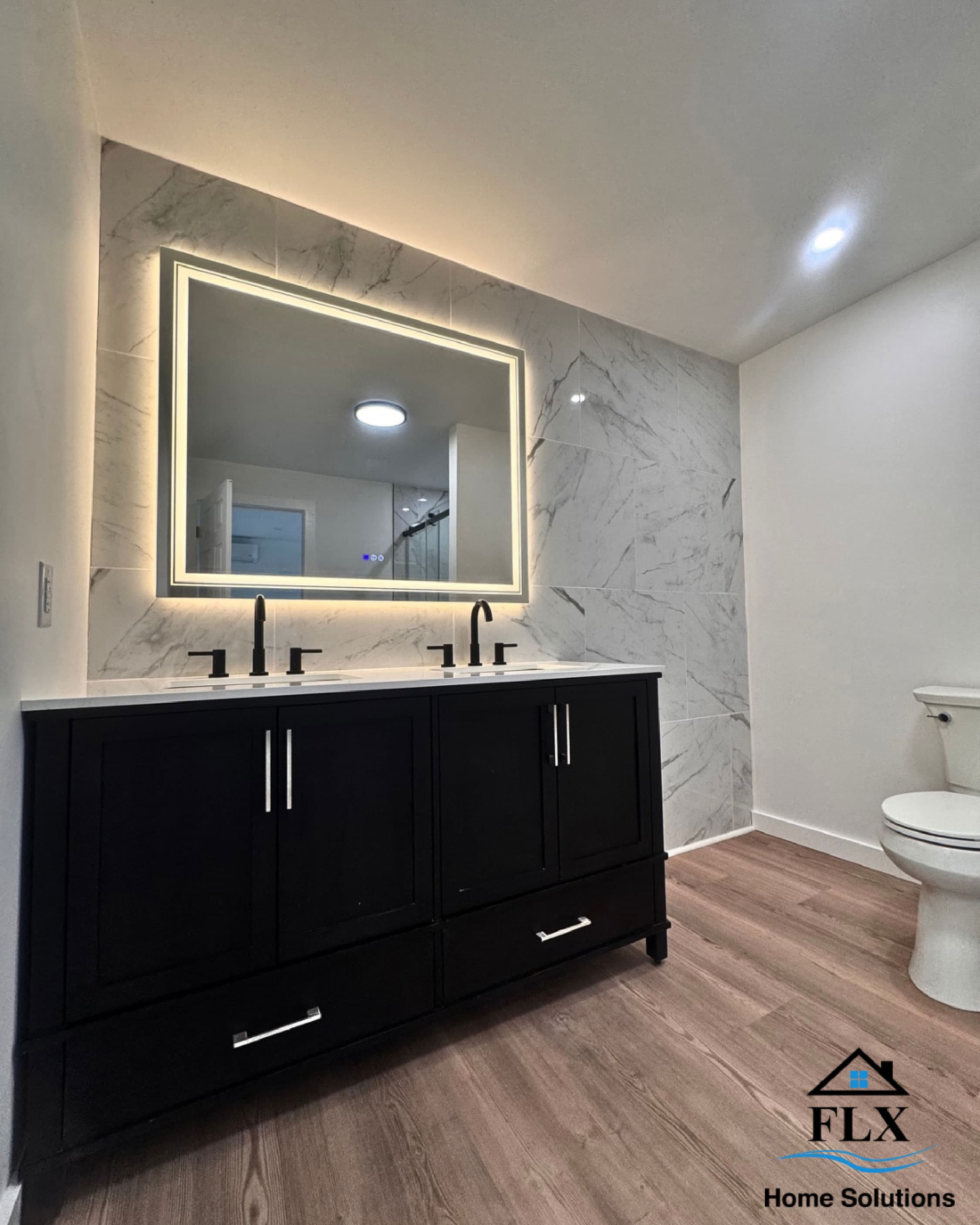 Modern bathroom with black double vanity, LED mirror, and marble tile accent wall