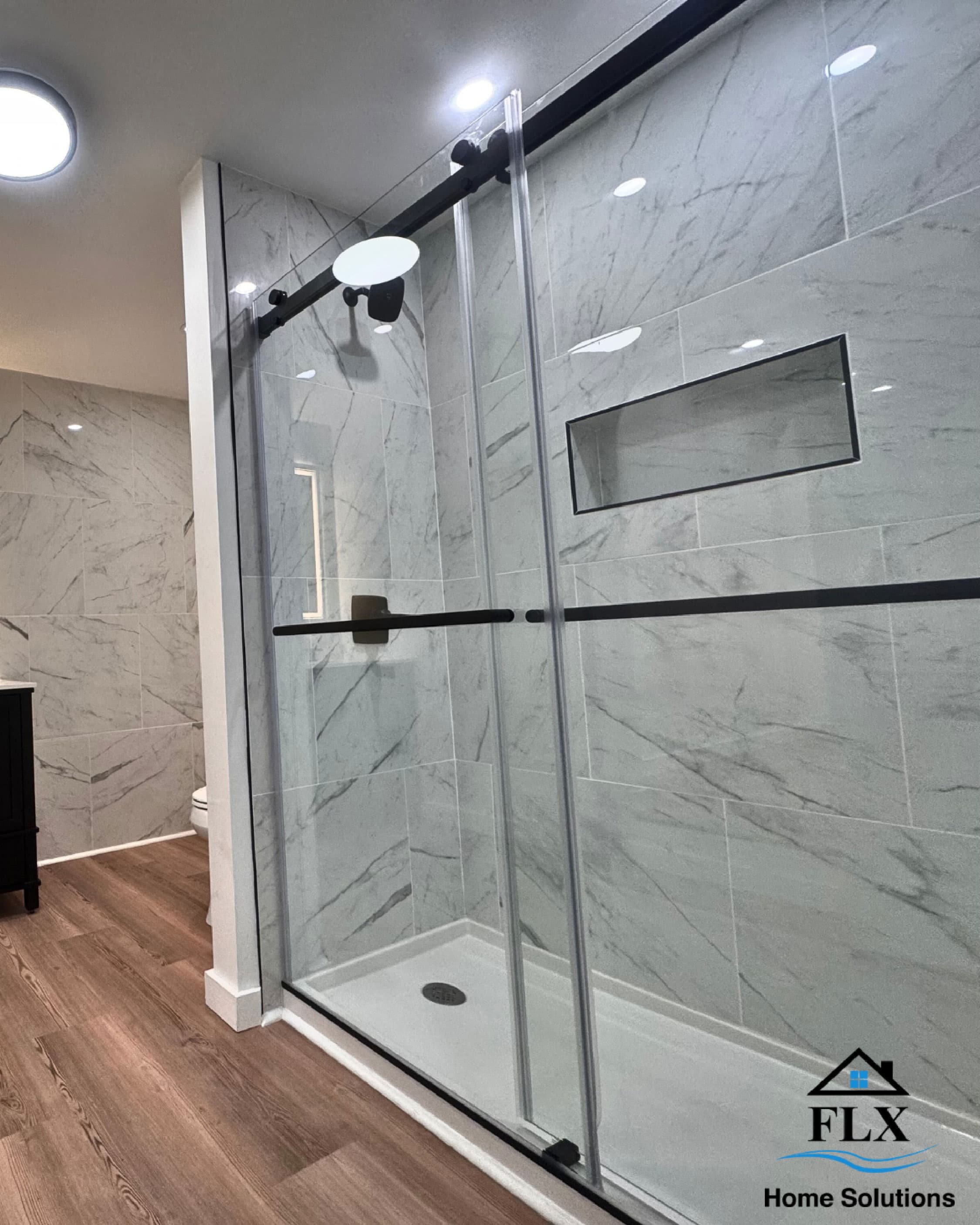 Walk-in shower with frameless glass doors and marble-look tile