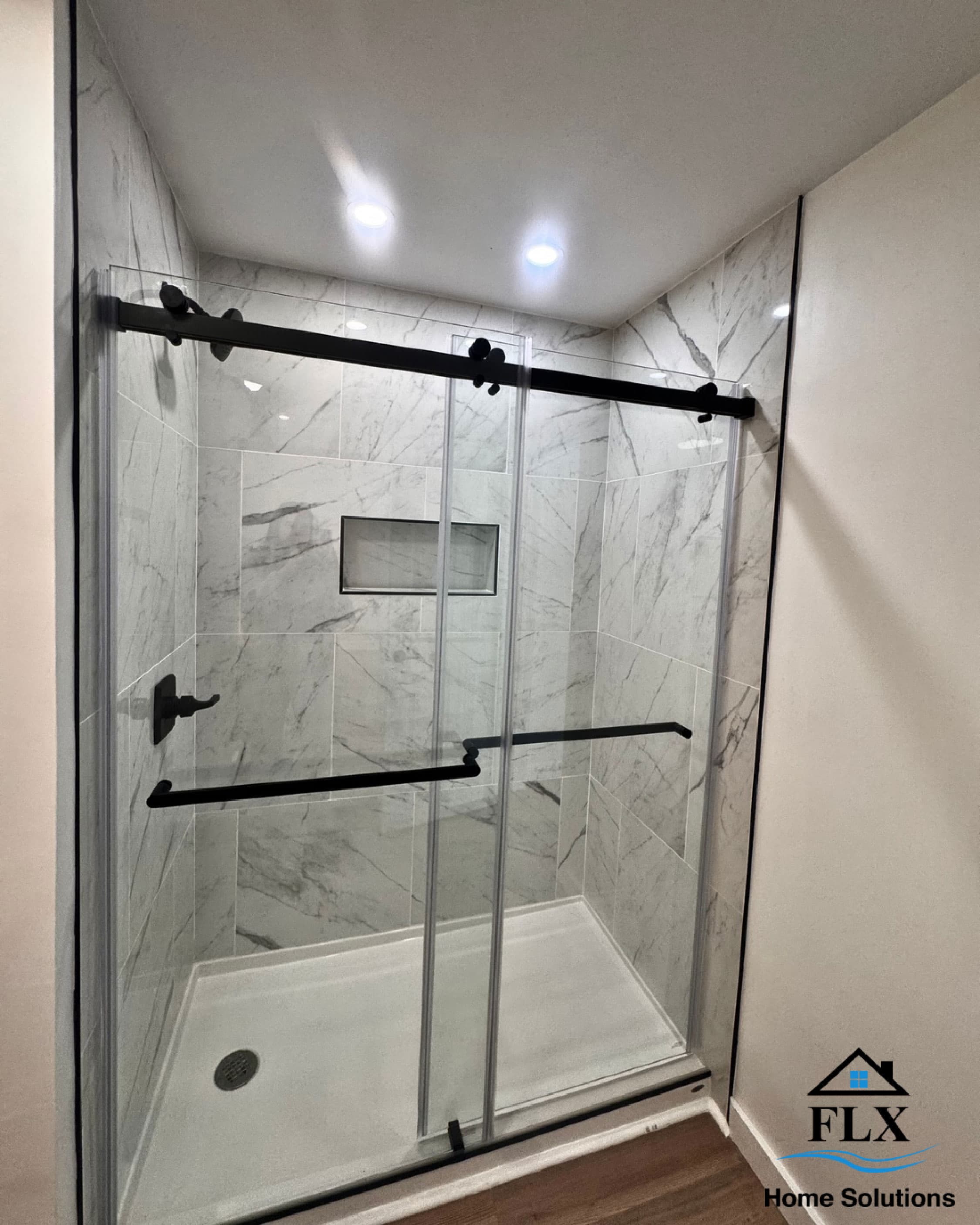 Glass shower with black sliding door hardware and marble tile surround