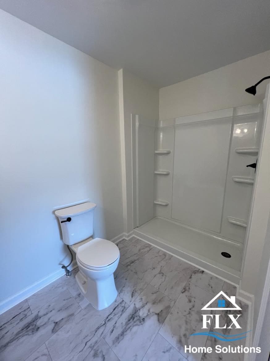 Remodeled bathroom with white shower surround, marble-look tile flooring, and white toilet