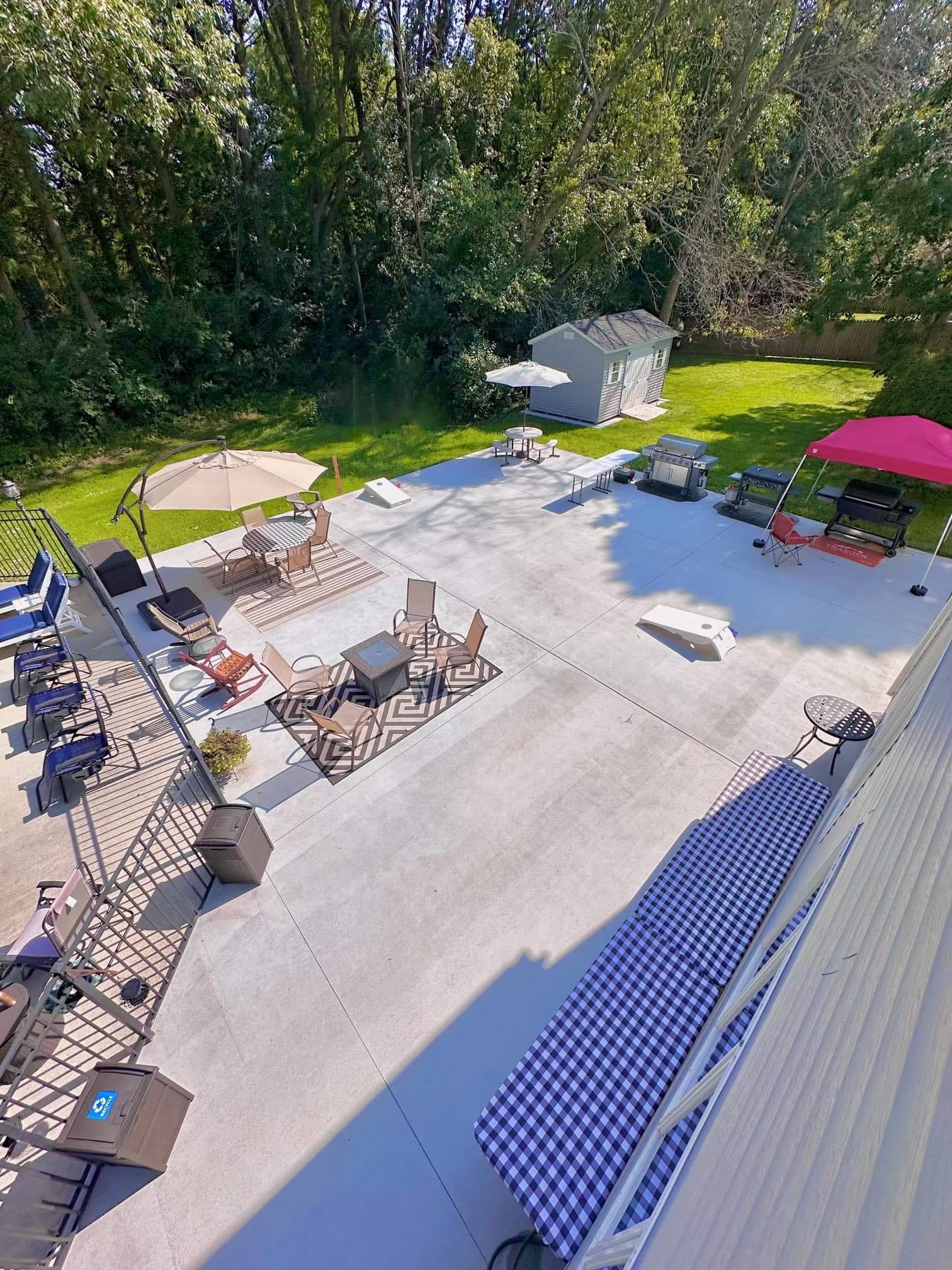 Aerial view of large concrete patio with outdoor furniture, shed, and lawn