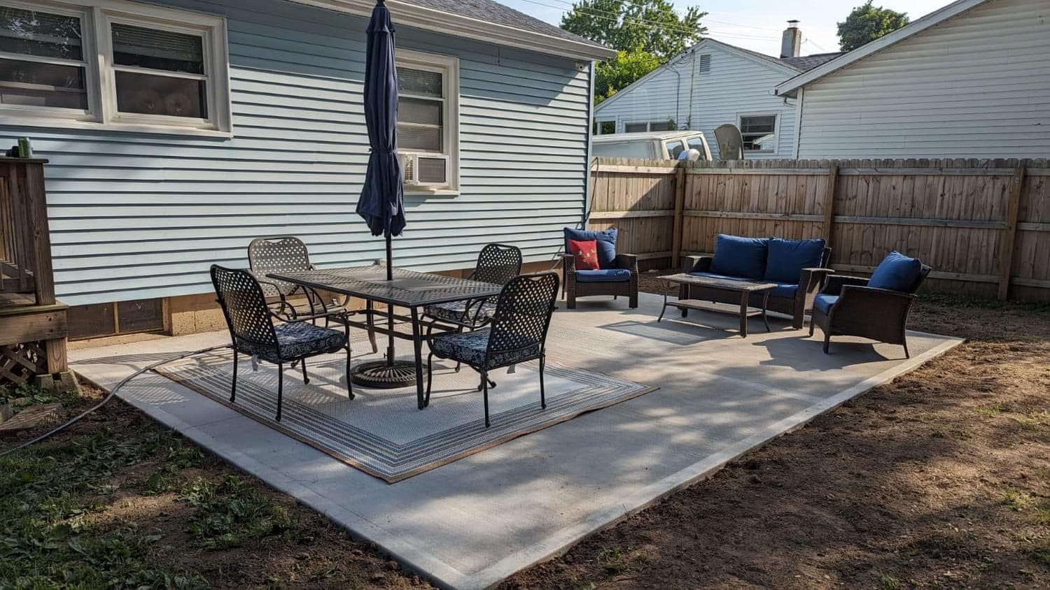 Concrete patio with dining set and lounge furniture in fenced backyard