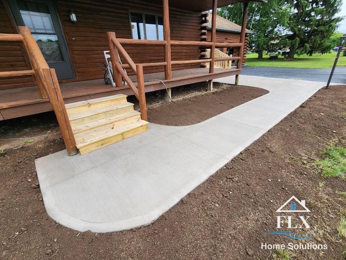 Concrete walkway leading to wood cabin deck with wooden stairs