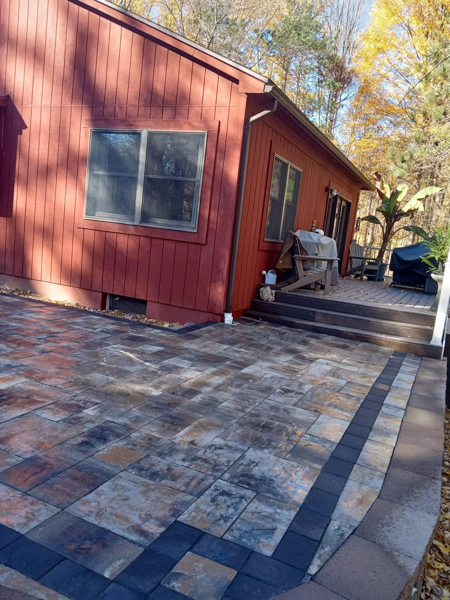 Multicolored paver patio with decorative dark border in front of red wooden house