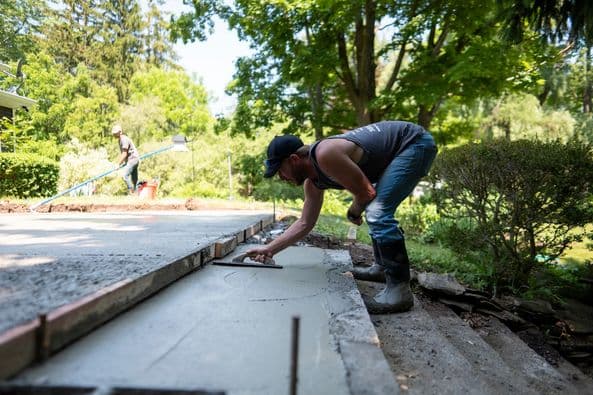 Worker smoothing fresh concrete on residential driveway