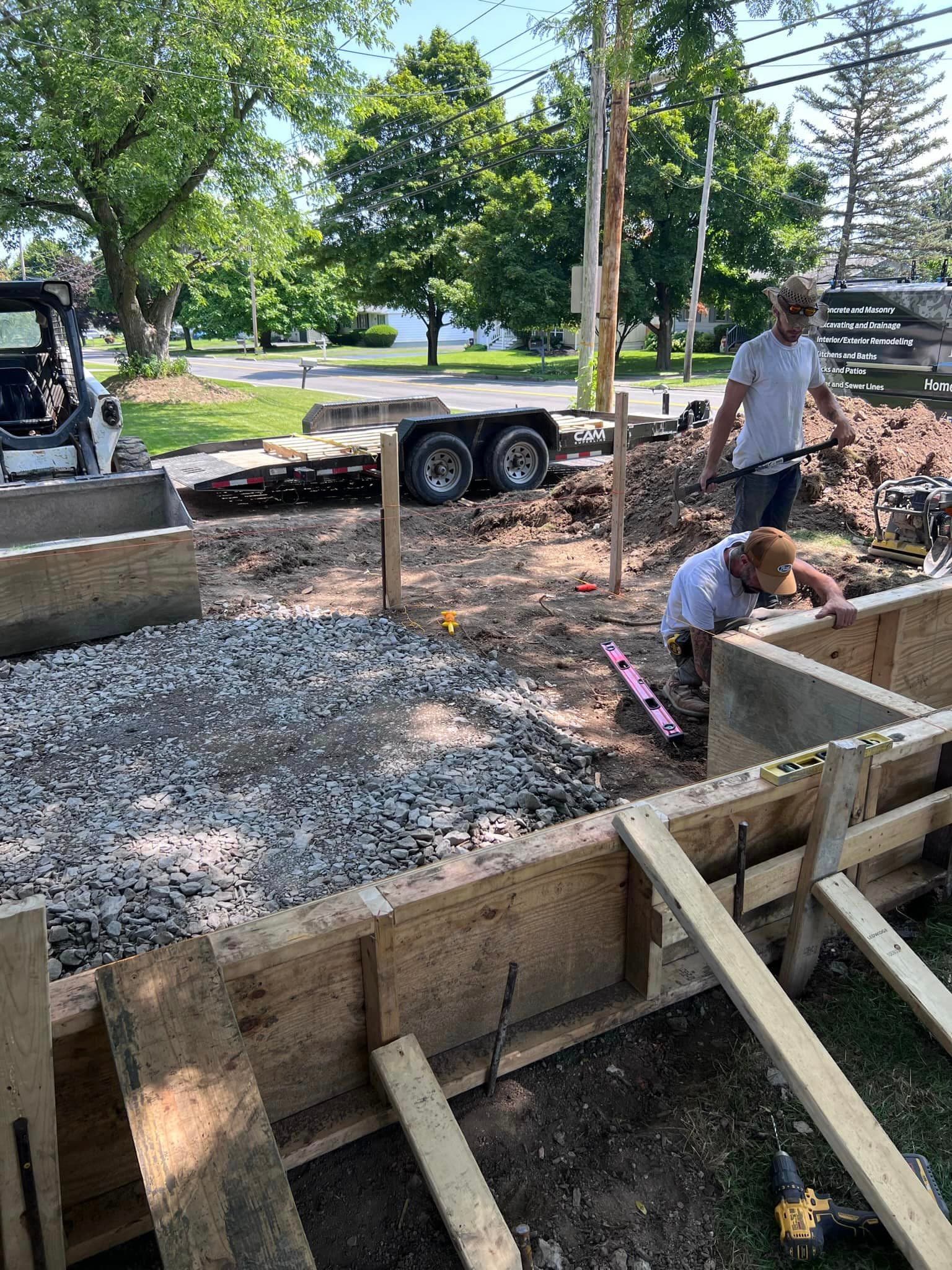 Workers preparing wooden formwork and gravel base for concrete driveway