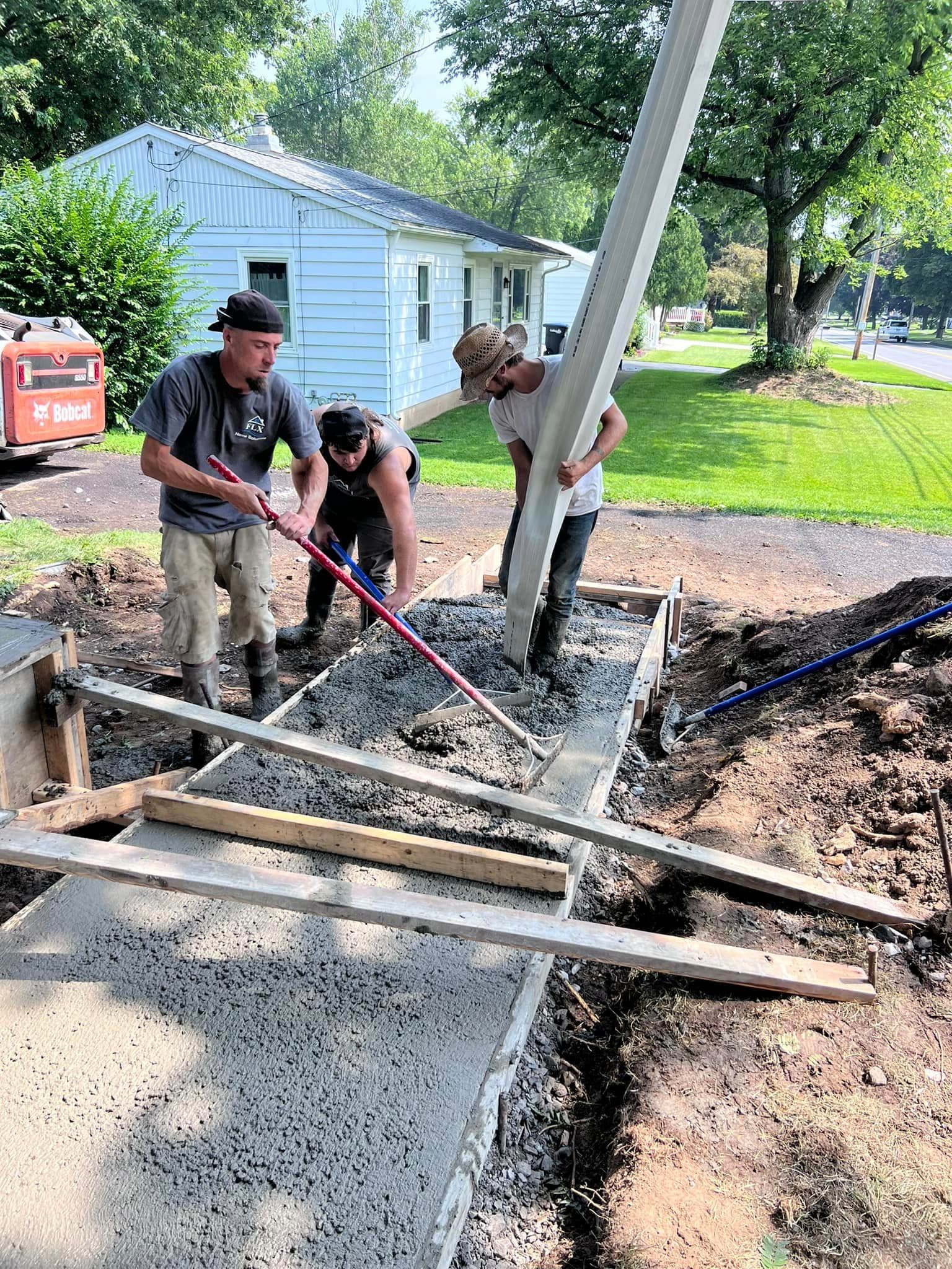 Three workers pouring and leveling concrete foundation with wooden forms