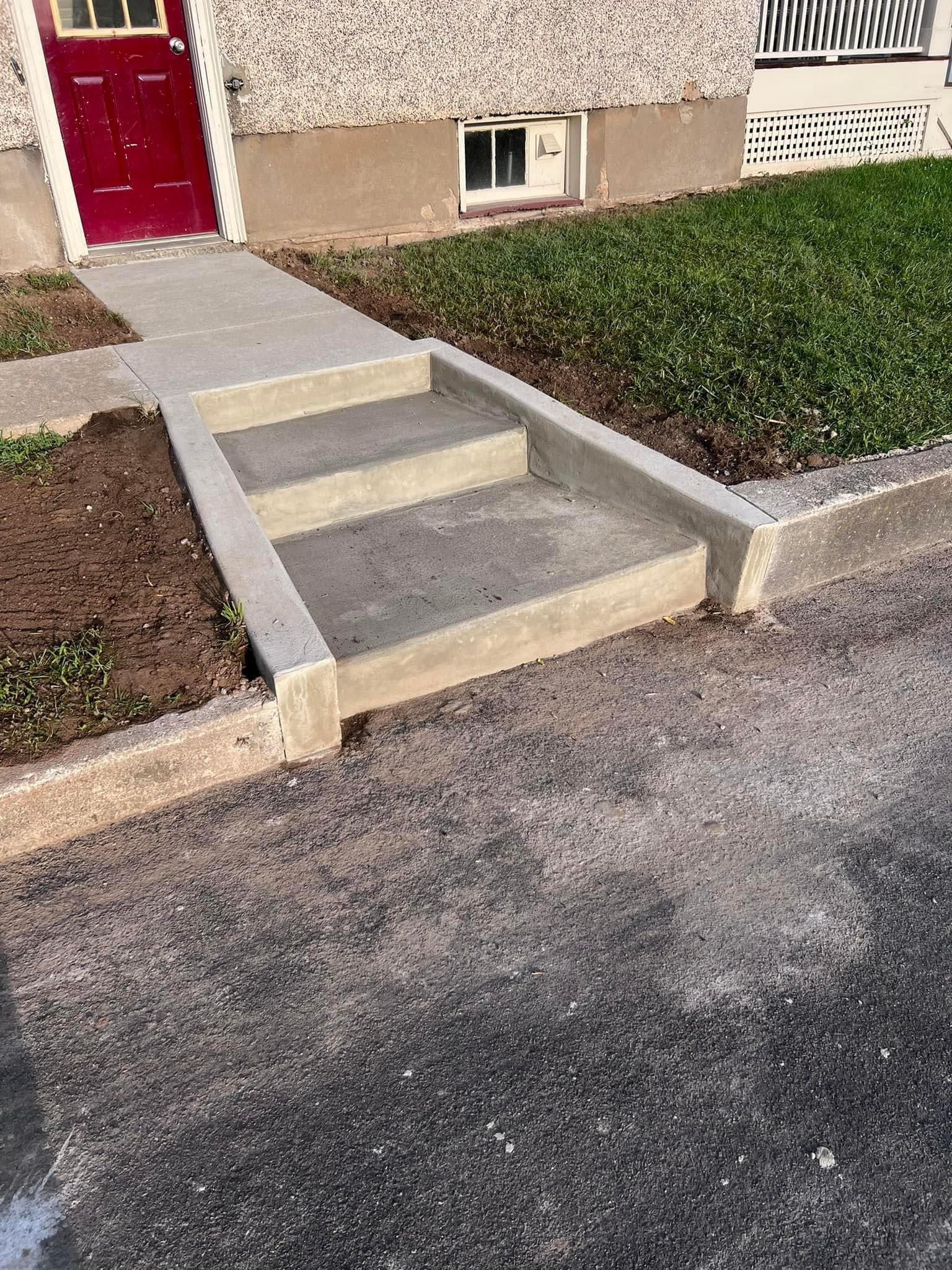 Concrete stairs leading from driveway to red front door with landscaping