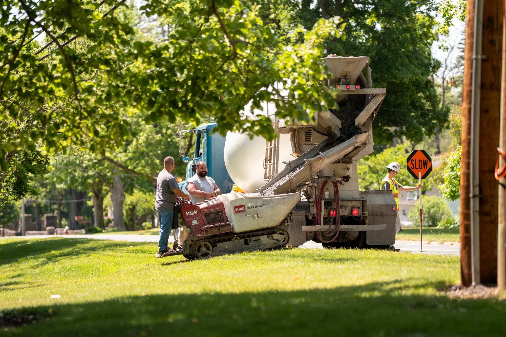 Concrete mixer truck with workers pouring sidewalk on residential street