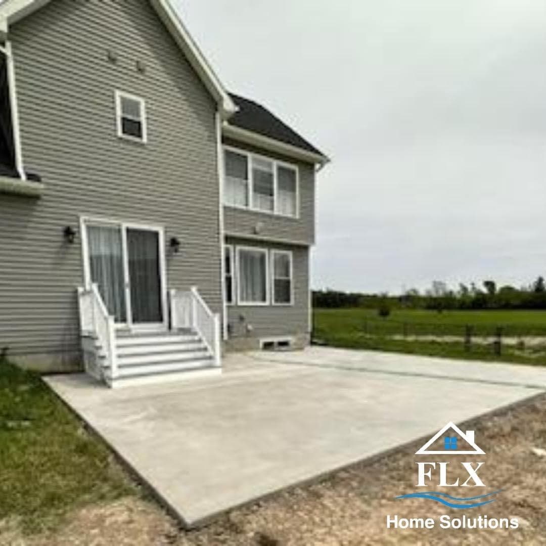 Concrete patio with stairs at gray two-story home with open field beyond