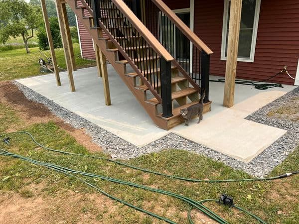 Concrete patio pads beneath wooden deck stairs with gravel borders