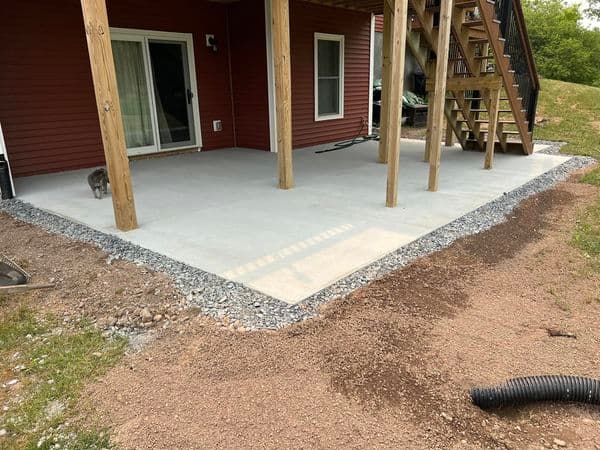 Freshly poured concrete patio under covered outdoor structure with gravel border