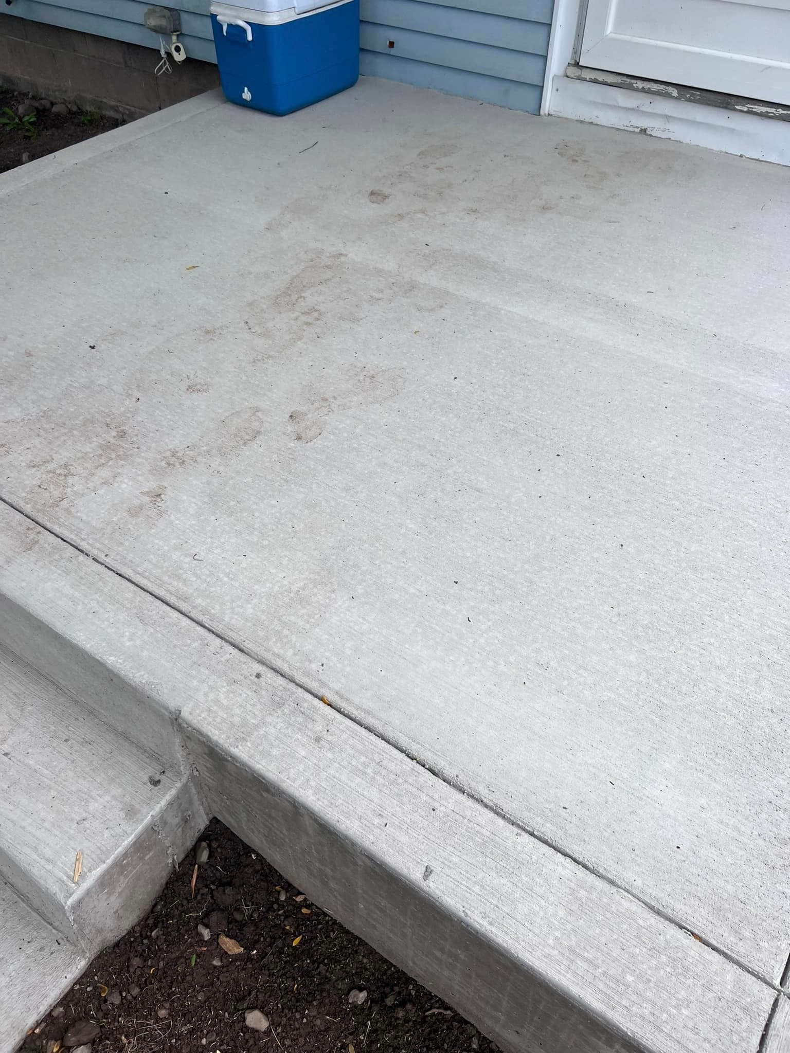 Freshly finished concrete porch with step leading to white door and blue cooler