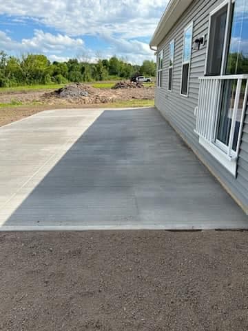 Freshly poured concrete slab beside white sided house with natural landscape