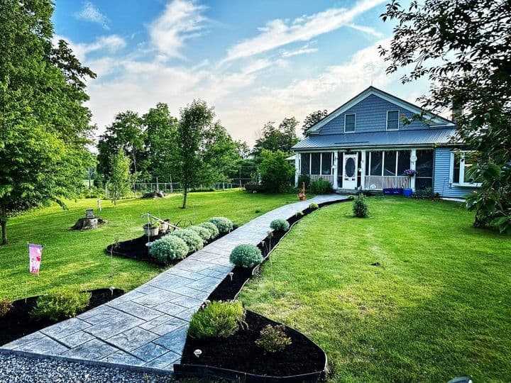 Concrete walkway leading to blue house with landscaped garden beds