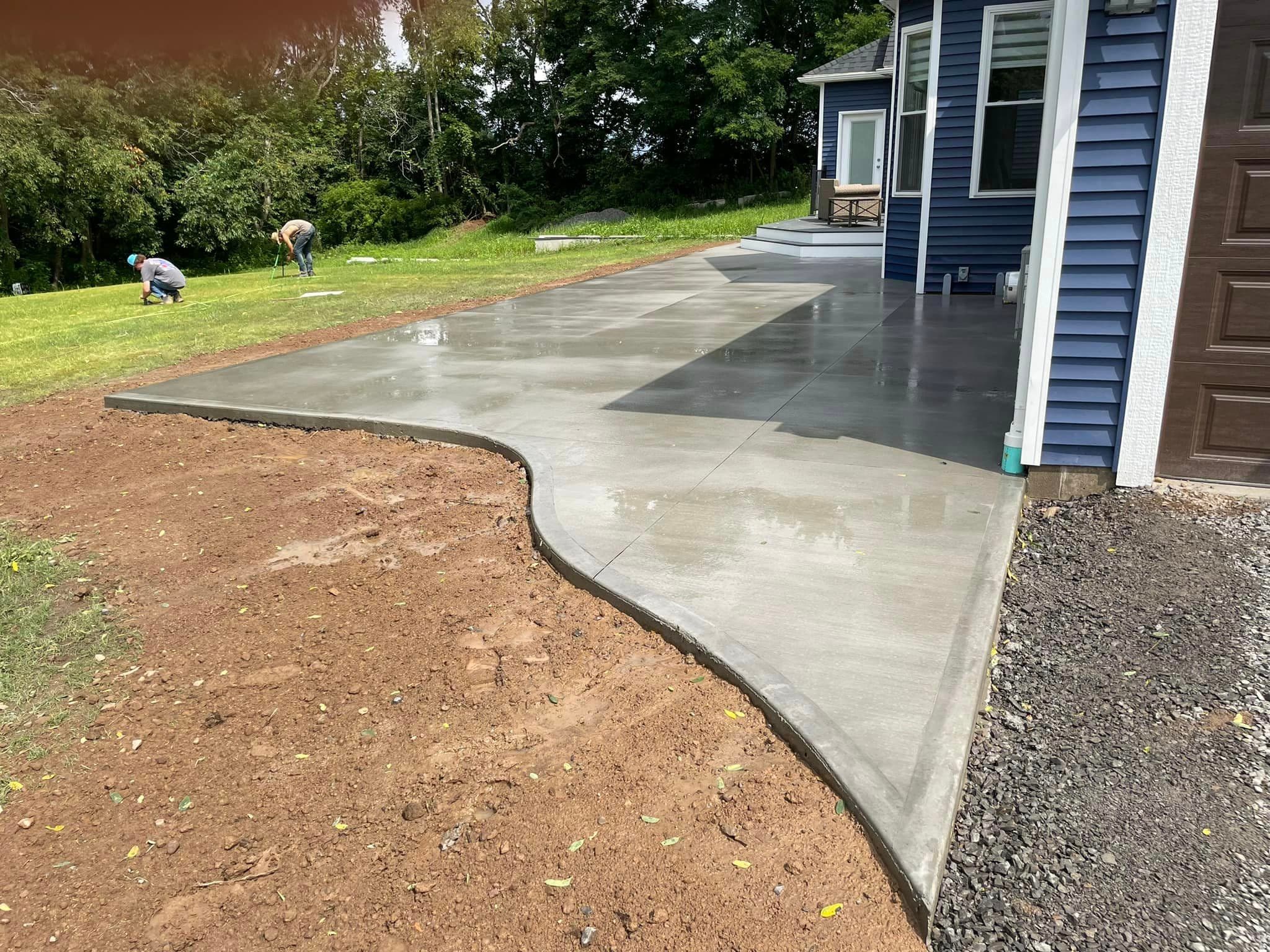 Newly poured curved concrete patio and driveway beside blue house