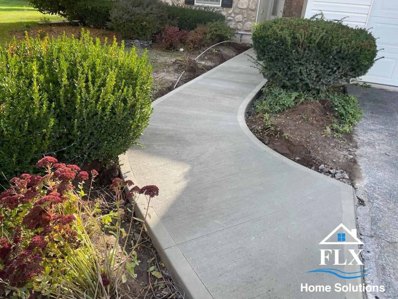 Curved concrete walkway leading to home entrance with landscaped garden beds