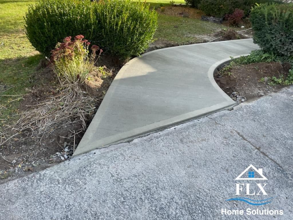 Newly poured curved concrete walkway connecting driveway to landscaped garden