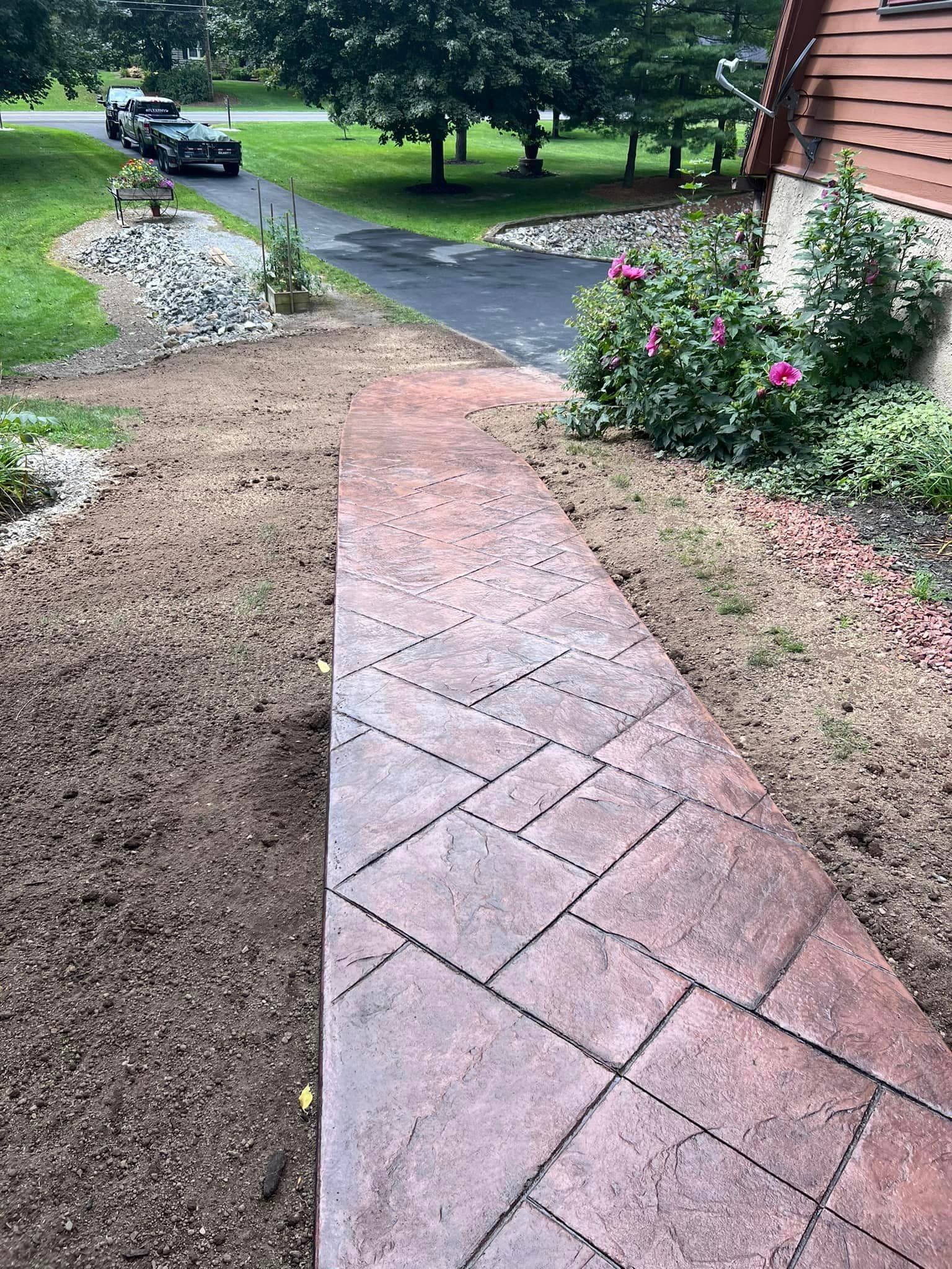 Curved paver stone walkway leading to house beside pink flowers