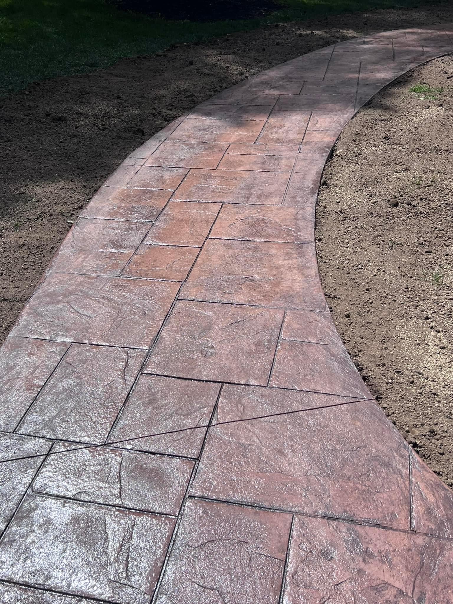 Curved stamped concrete walkway in reddish-brown tones on dirt base