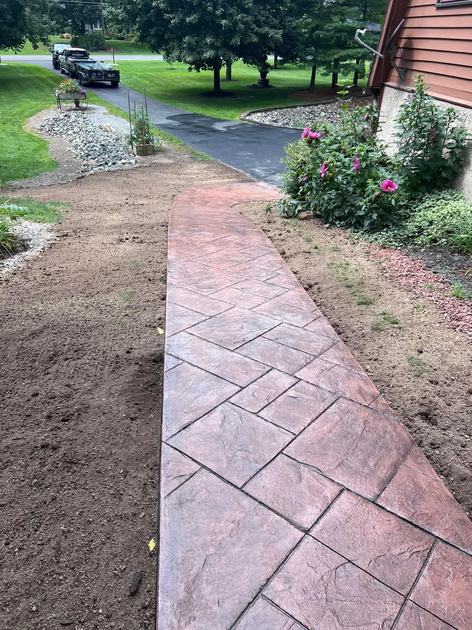 Curved stamped concrete walkway leading to house with pink flowers