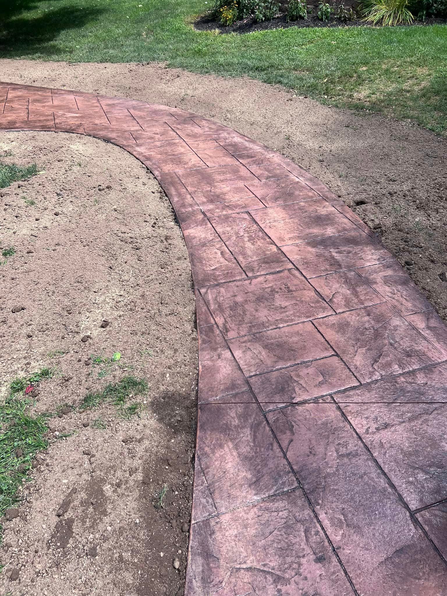 Curved stamped concrete walkway during installation with sand base visible