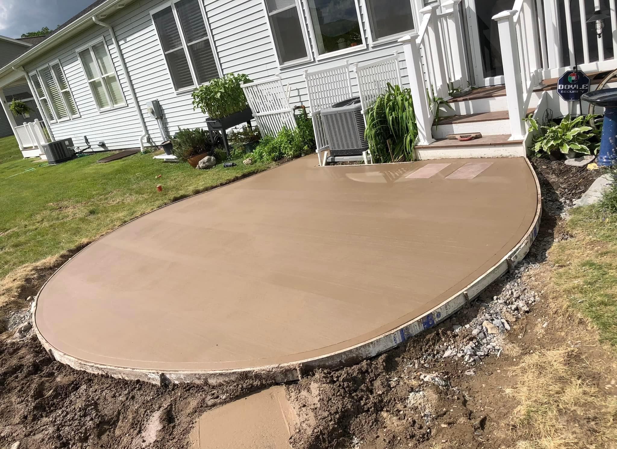 Newly poured tan concrete patio in front of white house with steps