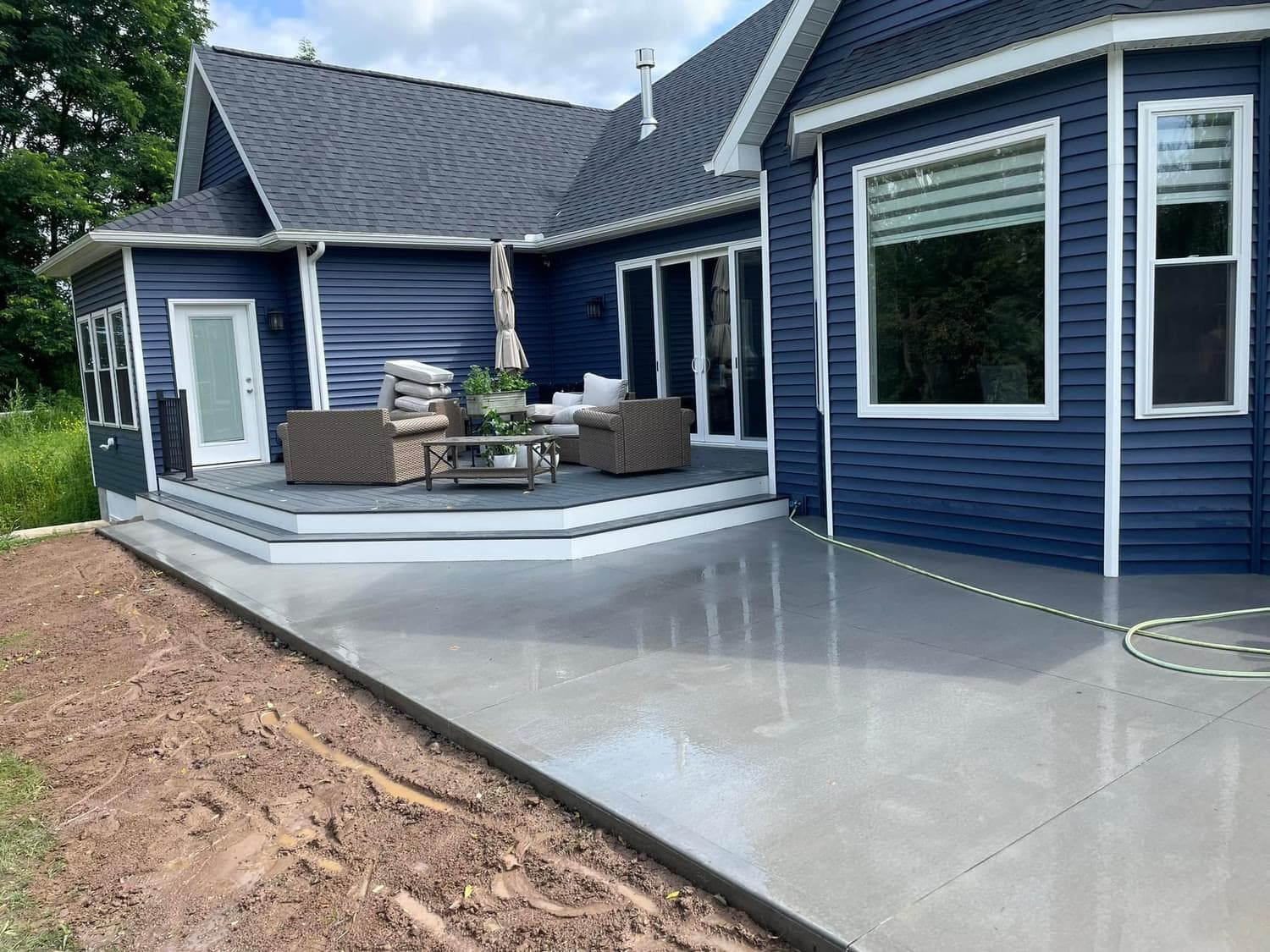 Fresh concrete patio beside blue house with elevated deck and patio furniture