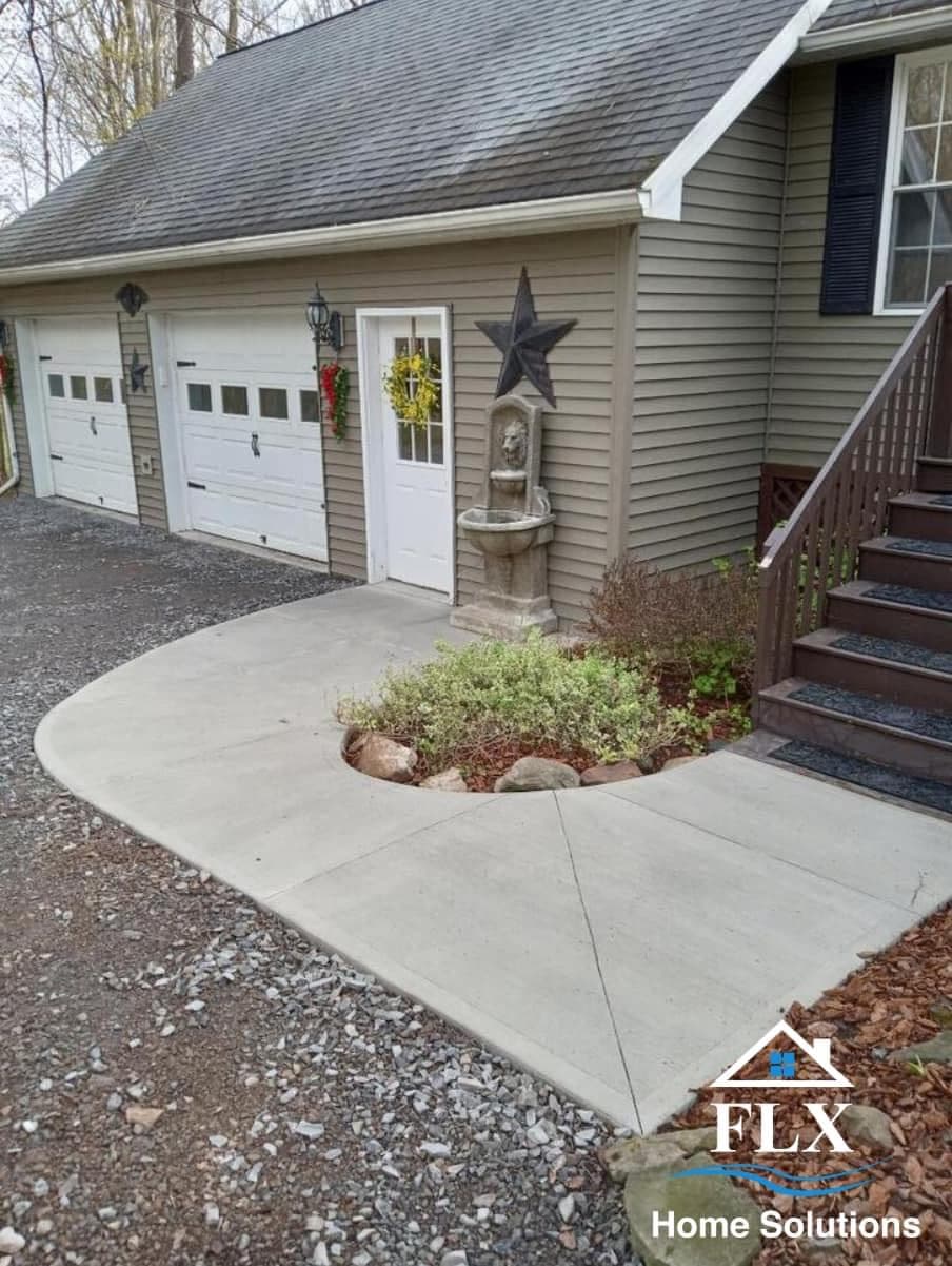 Concrete walkway beside garage with decorative fountain and garden bed