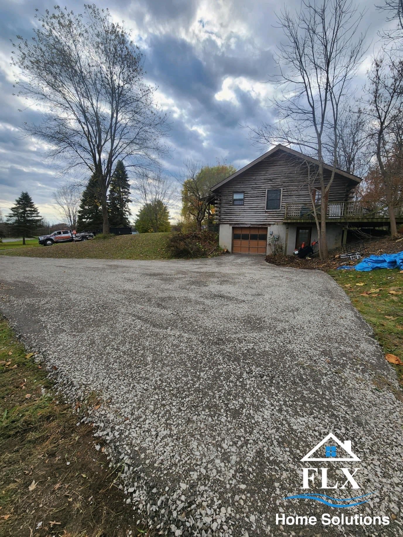 Gravel driveway leading to a two-story house with garage and deck