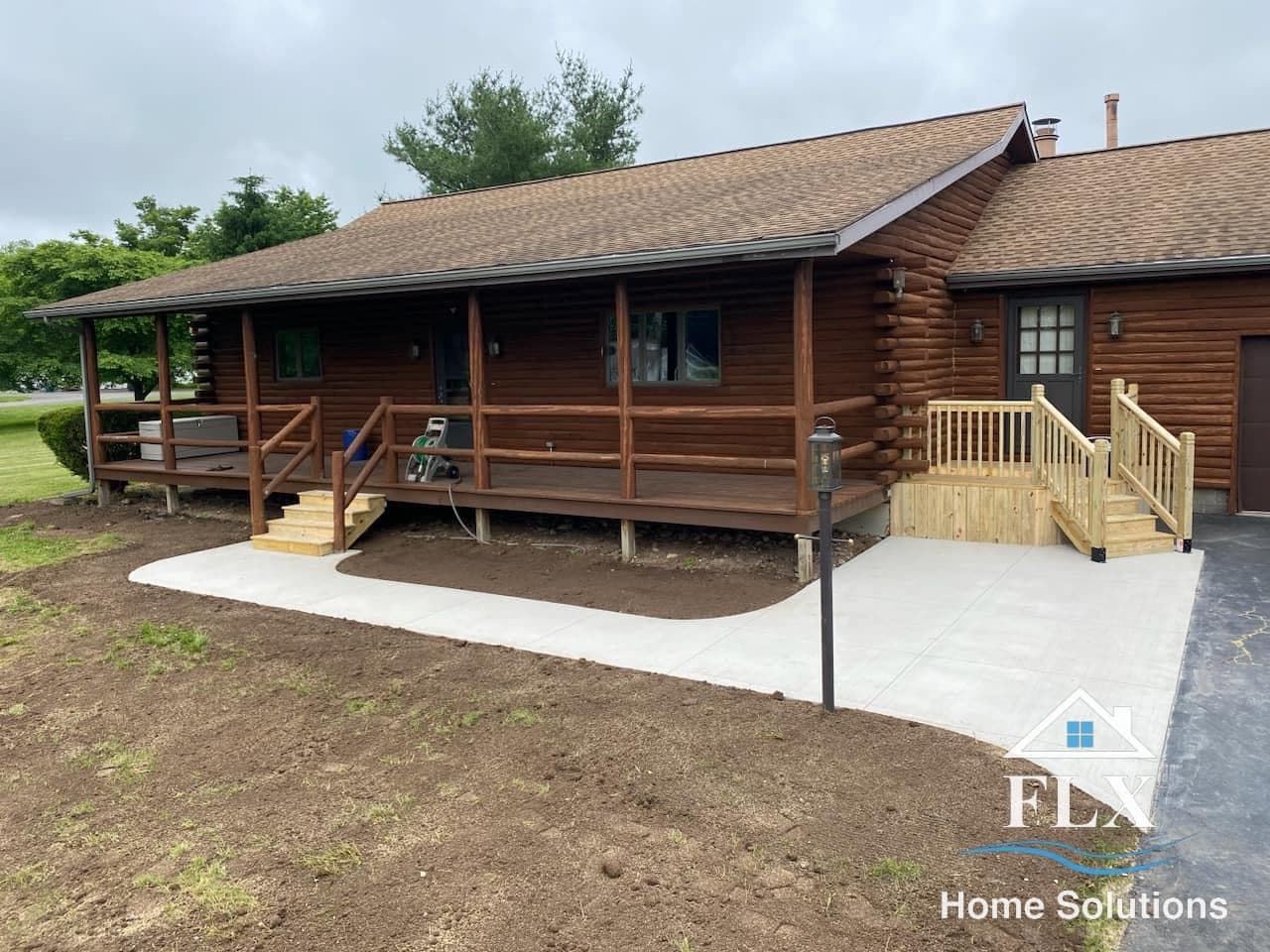 Log cabin with wooden deck and new concrete walkways leading to entrances