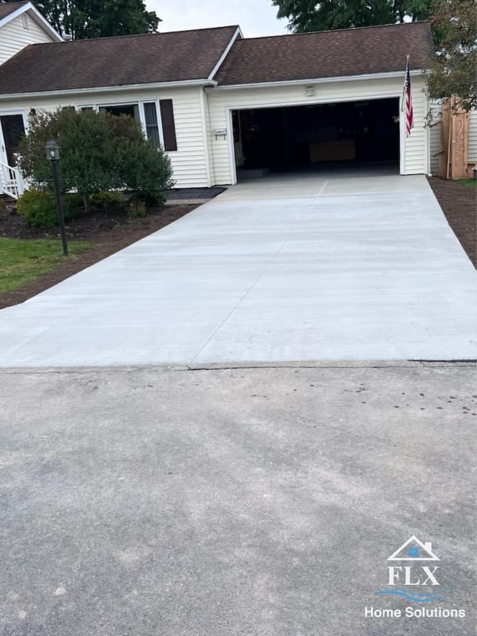 Freshly poured concrete driveway leading to open garage with dark mulch beds