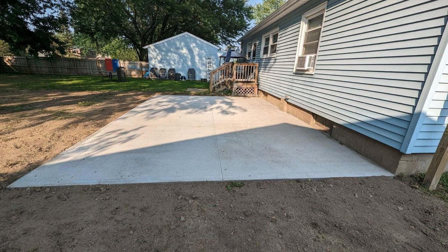 Freshly poured concrete driveway beside house with wooden deck stairs