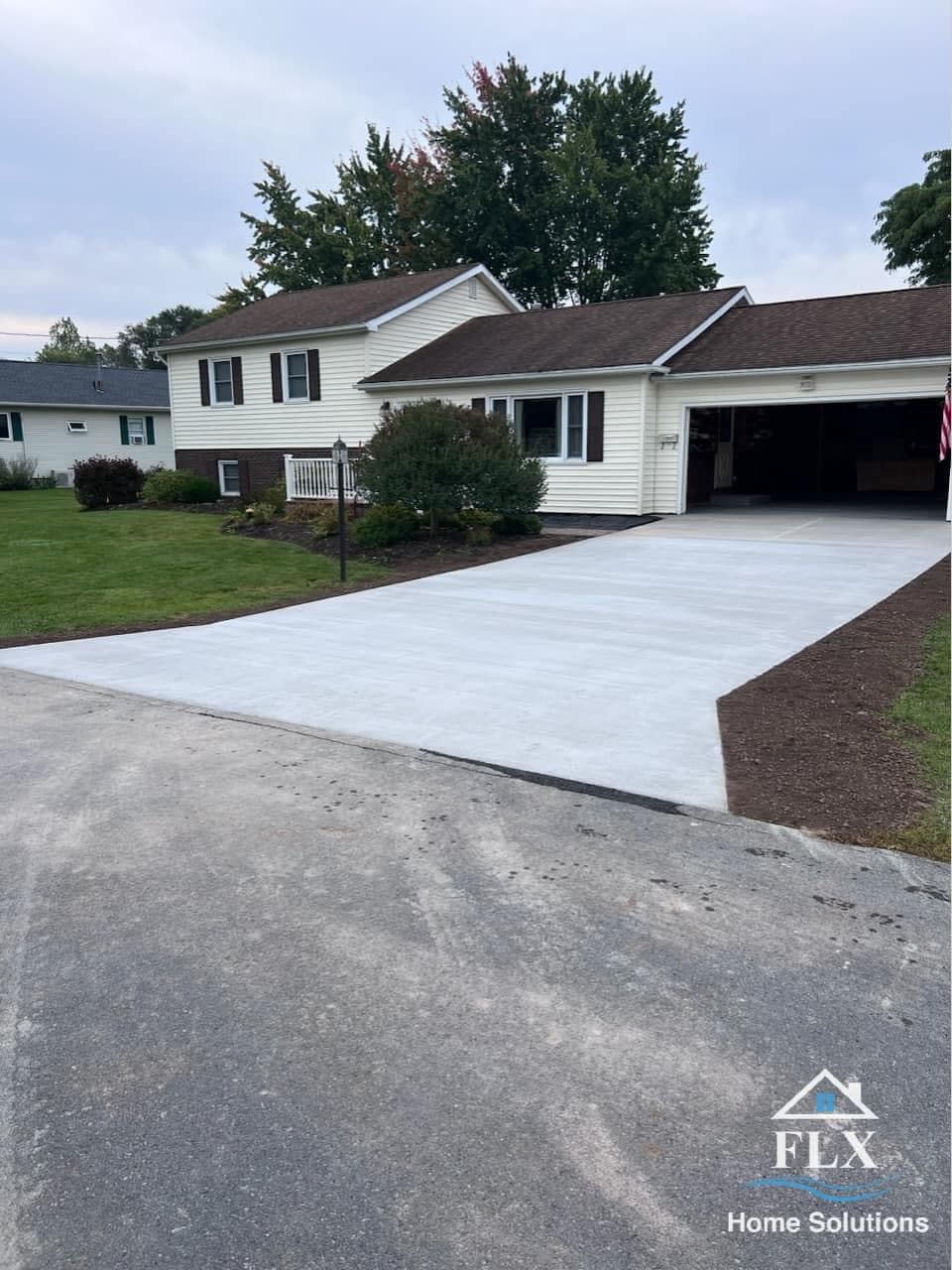 White concrete driveway leading to garage of beige house with brown roof